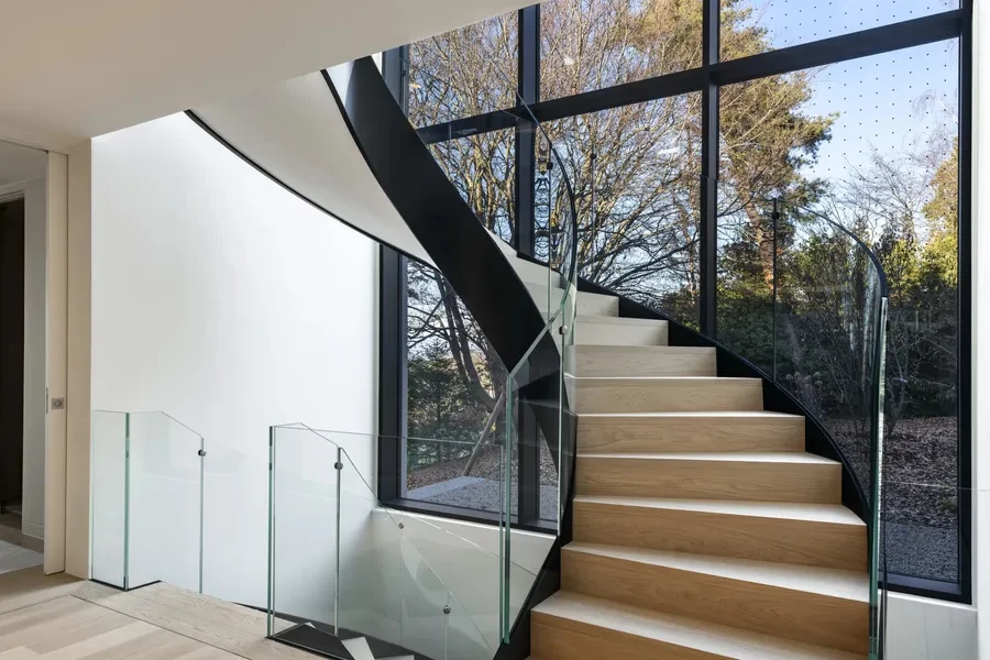 Cologny Geneva contemporary villa — sculptural curved staircase with glass balustrade and full-height glazing