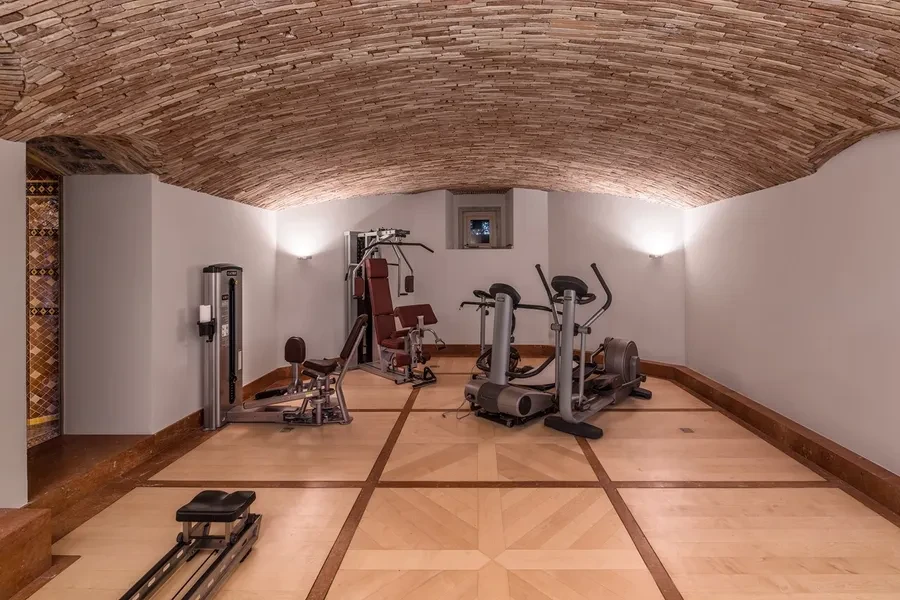 Cologny Geneva historic manor estate — fitness room with vaulted brick ceiling, gym equipment and parquet floors in the chalet